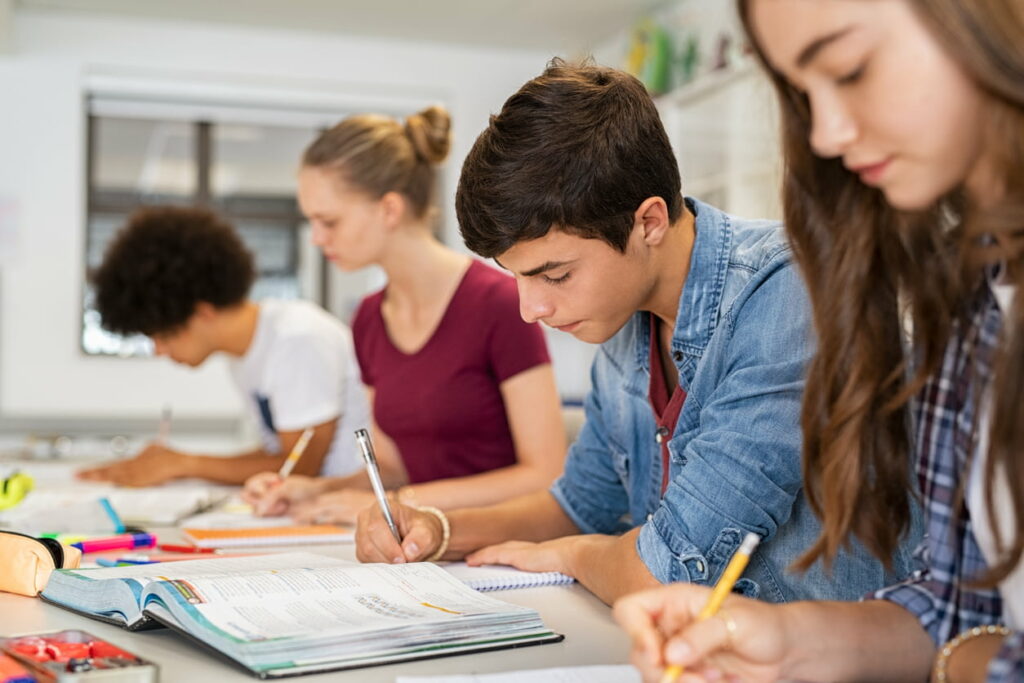 Estudantes concentrados estudando para o Enem em uma sala de aula, revisando materiais e fazendo anotações.